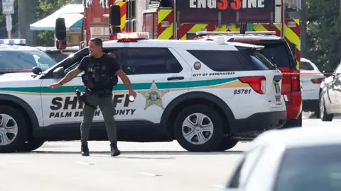 A police officer gestures in front of a sheriff's vehicle and a fire engine, with other cars to the right of frame, in West Palm Beach, Florida, U.S. September 15