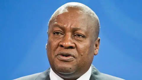 Ghanaian President John Dramani Mahama speaks at a press conference, with a blue backgroud behind him