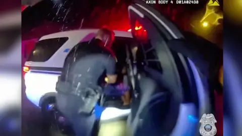 Two police officers are seen by their patrol car.