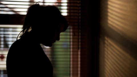 Woman in shadow standing in front of window blinds