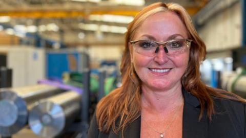 Andrea Wilson wears safety glasses on the shop floor of a factory with machines in the background