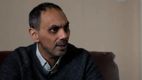 Ravinder Naga wears a grey jumper and shirt.