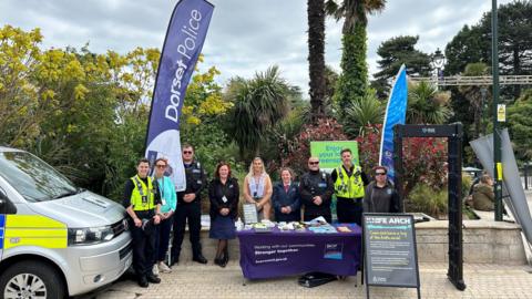 Police, council and other individuals gather at a stand in Bournemouth where they are stood next to a knife arch and a police vehicle