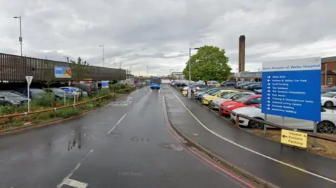 The entrance to a parking area at Grimsby's Diana, Princess of Wales Hospital, with direction signs, a small multi-storey car park and a bus travelling down the road.