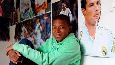 Kylian Mbappe sits on his bed surrounded by posters of Real Madrid forward Cristiano Ronaldo