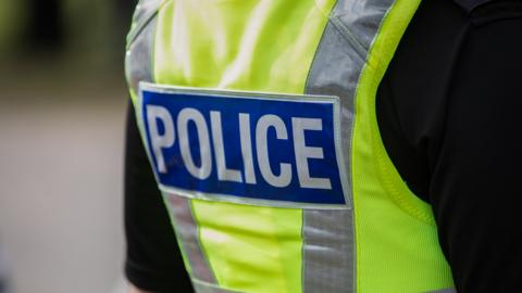 Back of a police officer's uniform - showing a green vest with police on the back