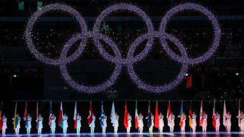 Olympic rings above a line of people holding flags from different countries