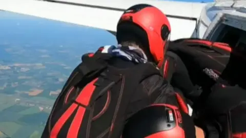 Two skydivers prepare to jump from a plane above countryside on a sunny day