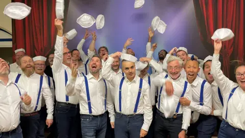 LGBTQ+ choir throw their hats in the air whilst dressed as sailors