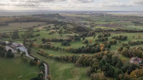 Aerial view of hills interspersed with patches of woodland and fields stretching into the distance. 