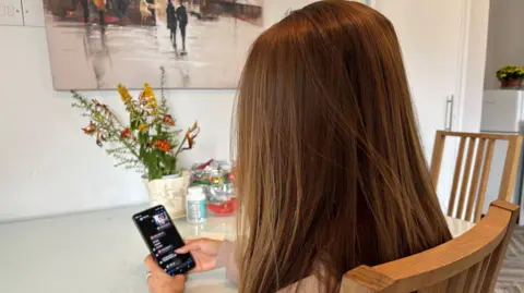 A woman with long brown hair from behind holding an iphone