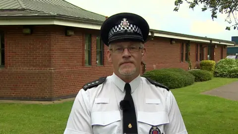 Ch Insp Jamie Gingell looking directly at the camera, standing in uniform in front of a red-bricked building