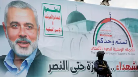 A soldier stands next to a banner with a picture of Hamas political leader Ismail Haniyeh