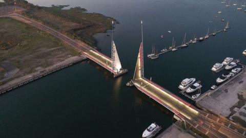 The two triangular sections of Twin Sails in the open position lit in gold and red with boats lined up on moorings