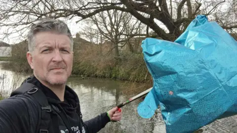 James Elliott James Elliott holding up a blue star helium balloon with a river backdrop