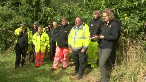 Twelve Cormac workers standing in a grassy and wooded area