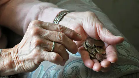 PA Media A pair of an elderly woman's hands holding coins. One hand has a wedding ring on a finger and she wears a wristwatch. 