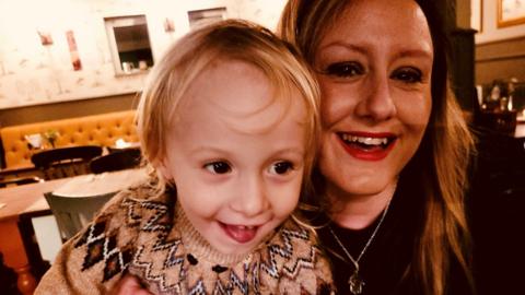 Becky Brookbank with her young son. They are sat in a restaurant and Becky smiles at the camera, while her son looks slightly away. 