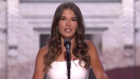 Kai Trump in white dress talking into a microphone