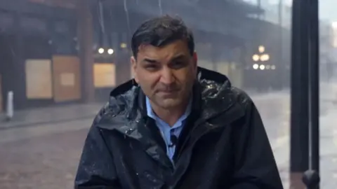 BBC News Correspondent Gordon Corera braces against the rain