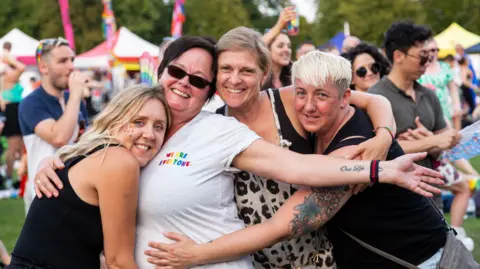 Four women looking towards the camera smiling and embracing