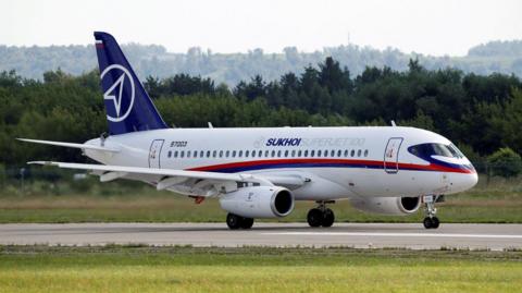 file image of Sukhoi superjet on a runway with trees in the background