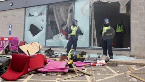 Police officers stand by a pile of rubbish and smashed glass