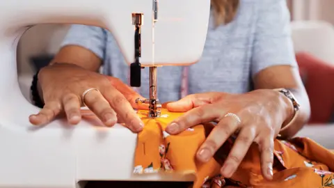 Stock image of a woman using a sewing machine to repair a colourful item of clothing