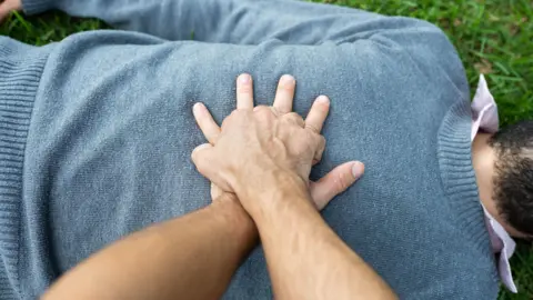 A man doing chest compressions on another man lying on grass