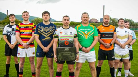 Players from eight teams standing in a line with new trophy