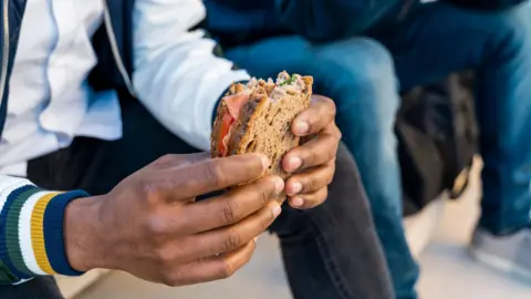 Close-up of a man holding a sandwich, sitting on stairs next to another man