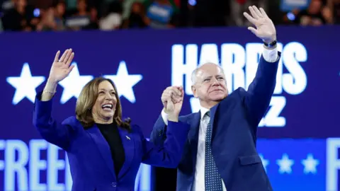 Vice President Kamala Harris and Tim Walz holding hands and waving at the DNC