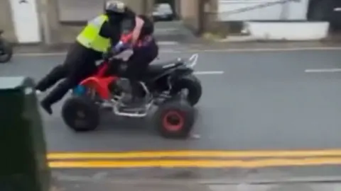 A police officer wearing a yellow vest being struck by a quad bike 