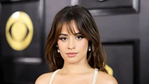 Camila Cabello at the 2023 Grammy awards, in front of a black board with the golden logo of the grammys