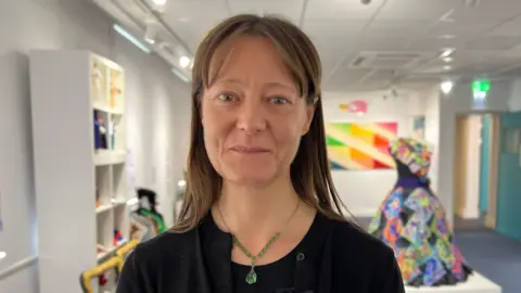 Frances Yeo pictured in the new gallery. She has long dark hair and wears a green jewelled necklace, and is smiling at the camera. 