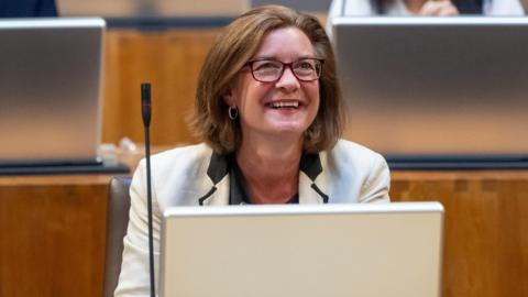 A smiling Eluned Morgan seated in the Senedd chamberamber