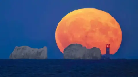 Gary Jacobs Large orange moon behind The Needles cliffs and lighthouse