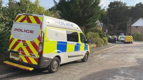 Island Echo Police van parked half up on a pavement with a smaller van further down to road homes can be seen on the left side