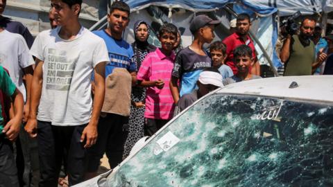Palestinians inspect a car damaged in an Israeli air strike in al-Mawasi, southern Gaza (16 July 2024)