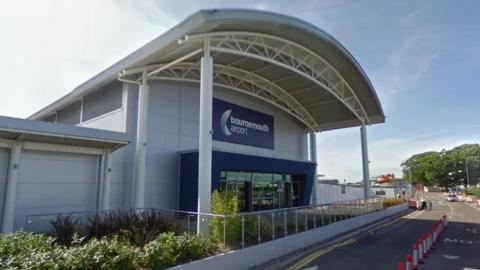 A picture of Bournemouth Airport's entrance - a large white building with a blue sign and blue doorway