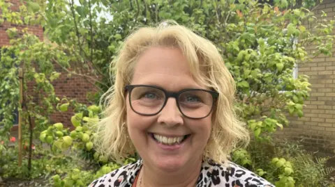 Chief executive of St Andrew's hospice smiling at the camera, she has blonde wavy hair cut in a bob style and is wearing a black and white leopard print top.