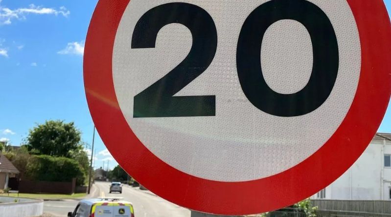 White and red 20mph sign with a backdrop of a residential street