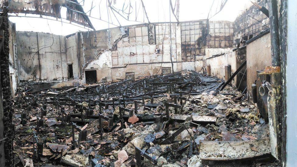 Charred remains of the cinema auditorium. The roof has collapsed and the floor is covered in charred debris