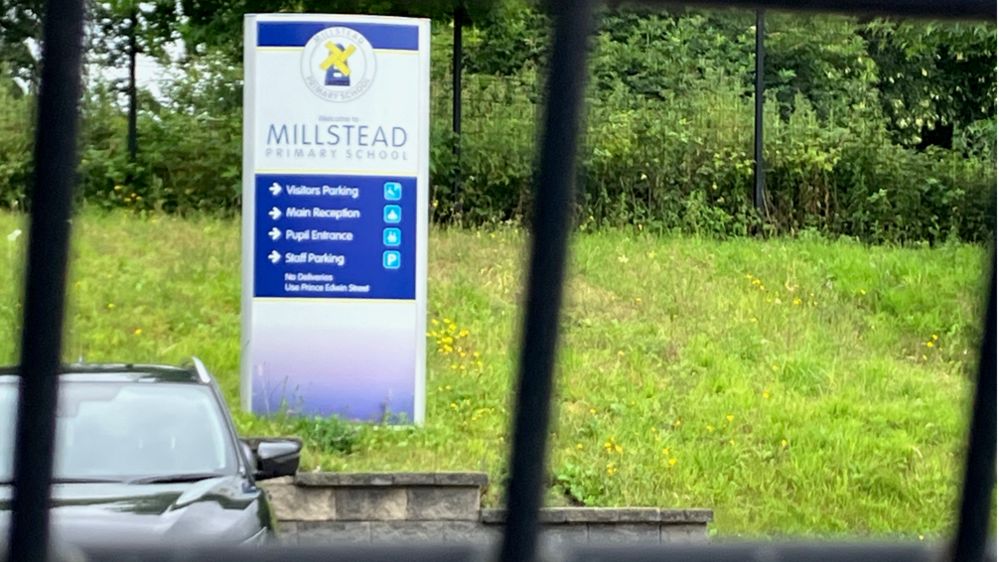 A sign saying Millstead Primary School at the entrance to the school, with a fence in the foreground