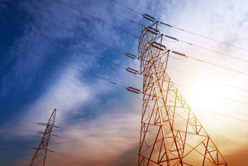 photo from the perspective of looking up to the top of electricity tower pylons with a colorful blue and yellow background in the sky