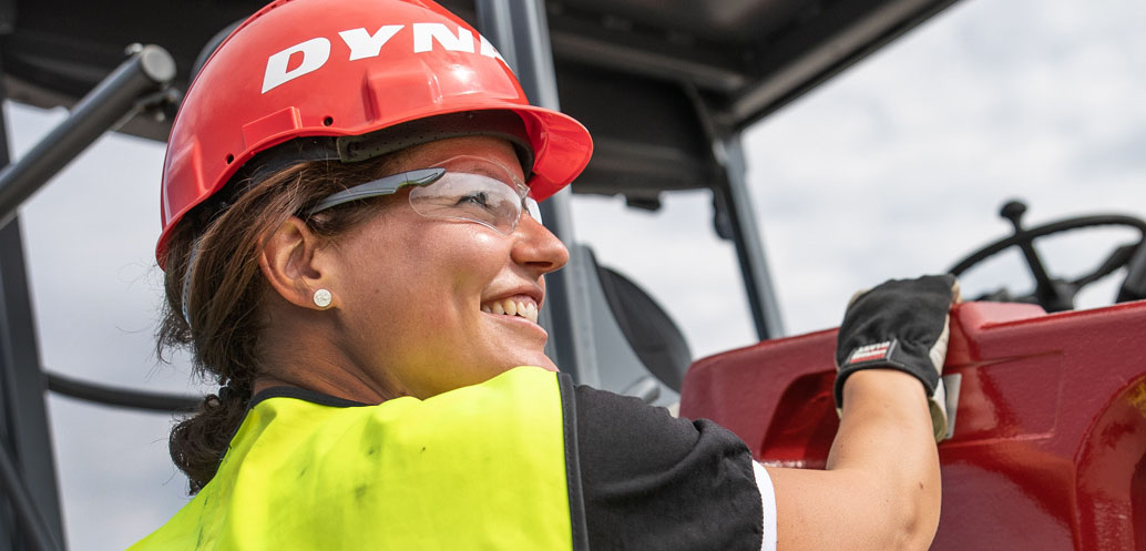 Female worker for Dynapac wearing a red helmet and protective glasses