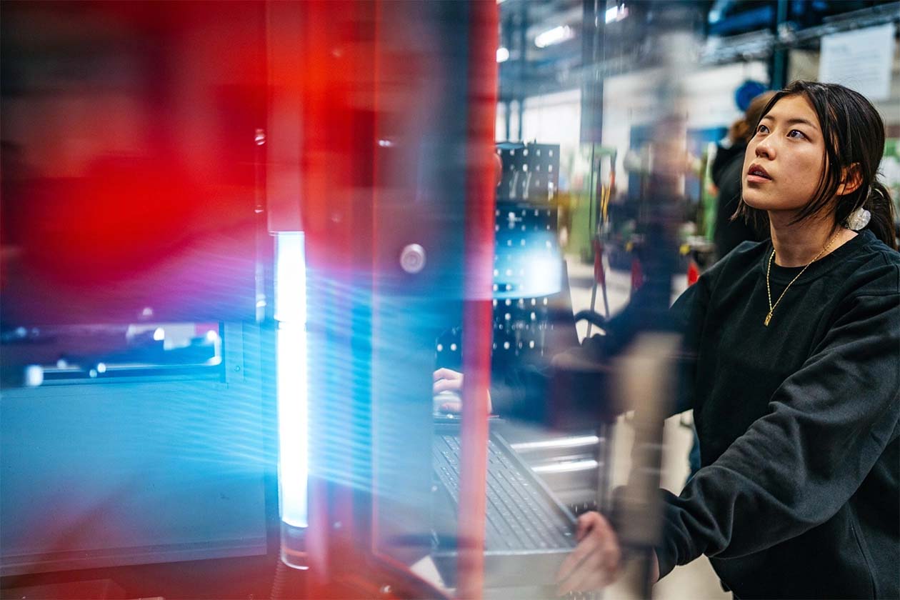 Female industrial worker with dark har standing by a big computer machine