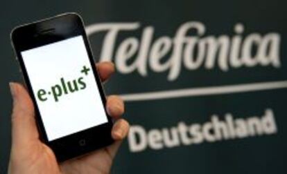 Fotograf&iacute;a de archivo que muestra una mujer sosteniendo un tel&eacute;fono inteligente en cuya pantalla aparece el logotipo de E-Plus frente a un cartel de Telef&oacute;nica Deutschland, en M&uacute;nich, Alemania. 