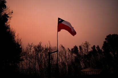 A Chilean flag stands amid charred trees under a red sky caused by wildfires in Santa Juana, Chile