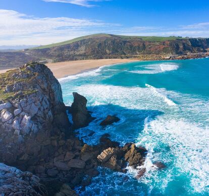 Ejemplo de playa de arena blanca, tan asilvestrada como peligrosa para el baño. Cuando el mar castiga Liencres, Usgo atrae a los surfistas de la comarca, entre ellos a los del Special Surf School (specialsurf.com), del tres veces campeón de Europa Dani García. Las caribeñas franjas azul claro en el agua son producto de la solución salina vertida por la empresa Solvay. <BR></BR>En la imagen, vista del arenal de Usgo, una playa encajada entre acantilados en la localidad cántabra de Miengo.